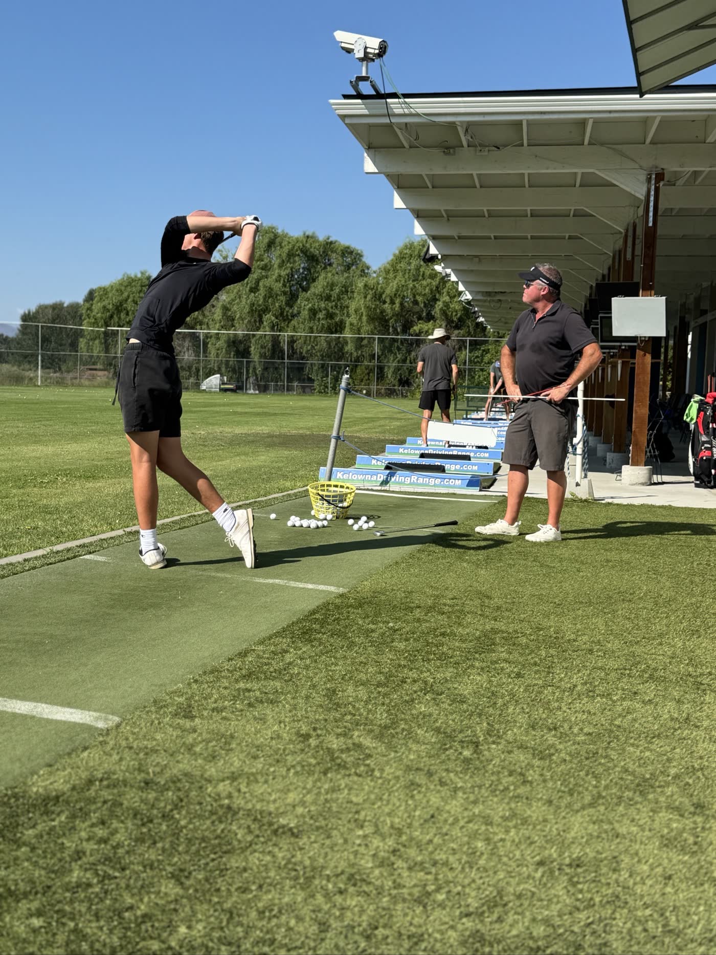 Golf lesson at Kelowna Driving Range — a student holding his finish as PGA of Canada coach Steve Lawrence watches